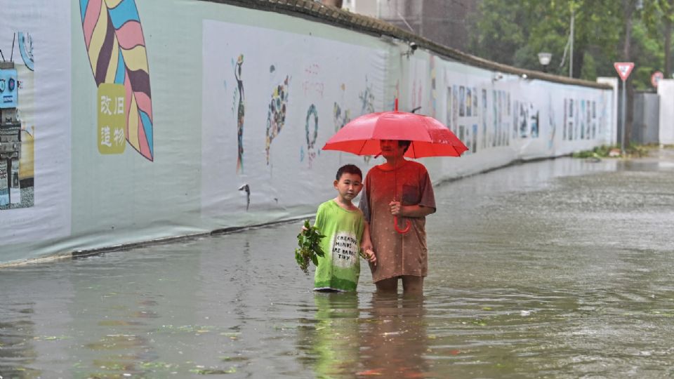 ZHEJIANG. Una mujer y un niño cruzan una calle inundada, por las fuertes lluvias. Foto: AFP