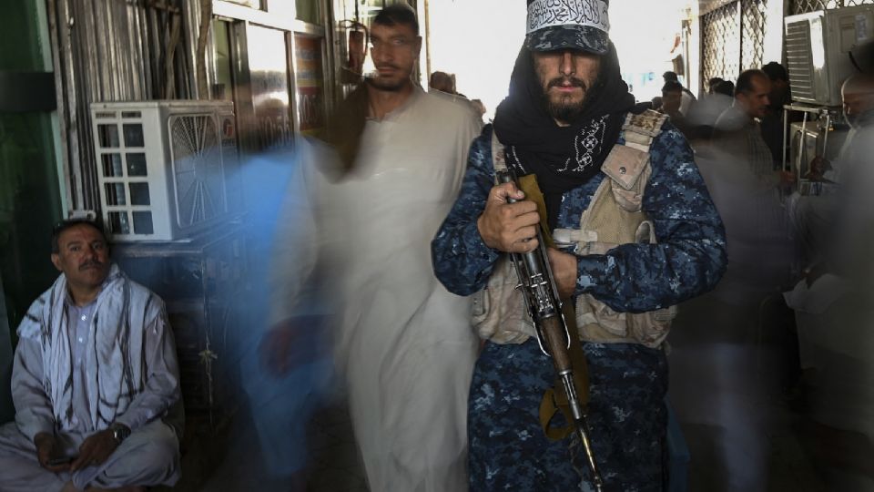 Combatiente talibán montaba guardia al pasar gente por una tienda de cambio de divisas.