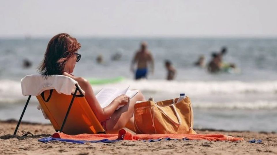 Mujer lee a la orrilla de la playa en un día de asueto.