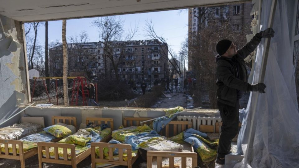 Un hombre retiraba una cortina de una escuela dañada en Kiev. FOTO: AP