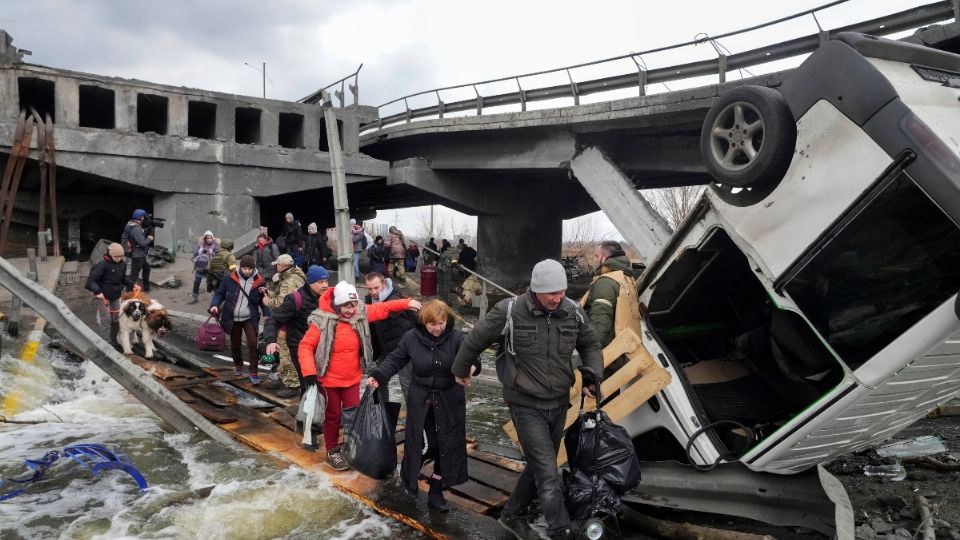 Personas cruzan un camino improvisado debajo de un puente destruido, mientras salen de Irpin cerca de Kiev