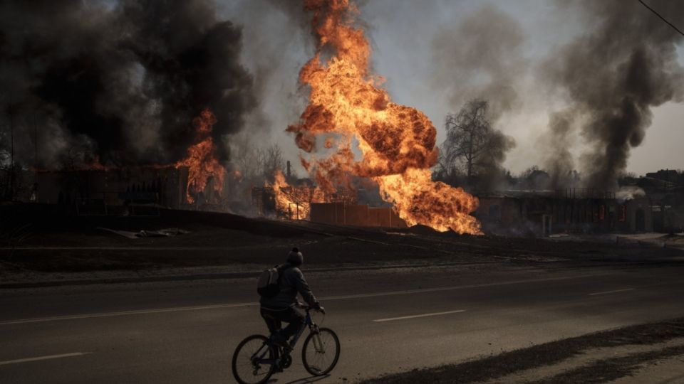 Un hombre pasa con su bicicleta junto a un edificio envuelto en llamas en Járkov el 25 de marzo. FOTO: AP