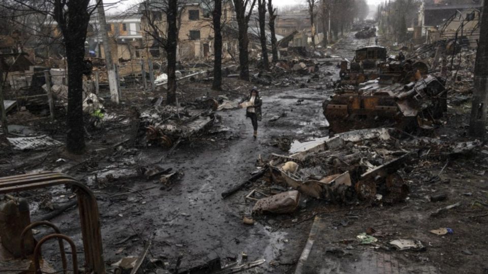 Una mujer camina entre vehículos blindados rusos destruidos en Bucha. FOTO: AP