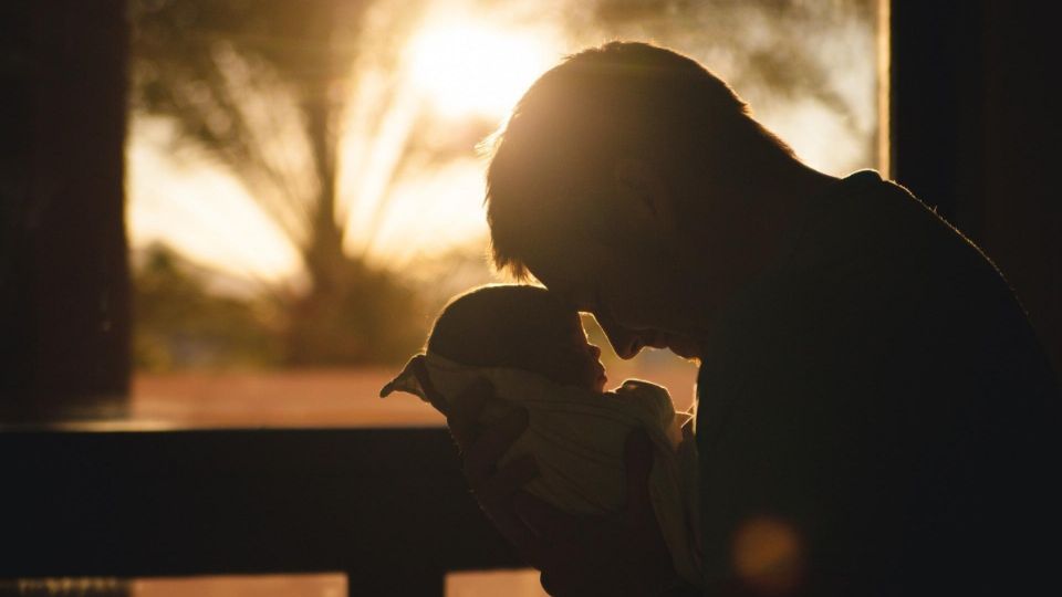 Padre sostiene a uno de sus hijos entre sus brazos.