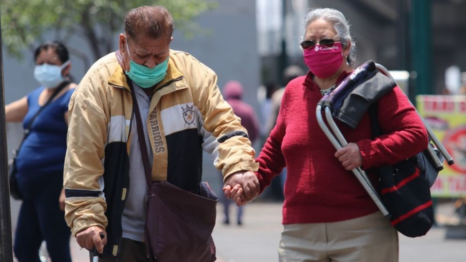 Dos adultos mayores se ayudan a caminar por la calle.