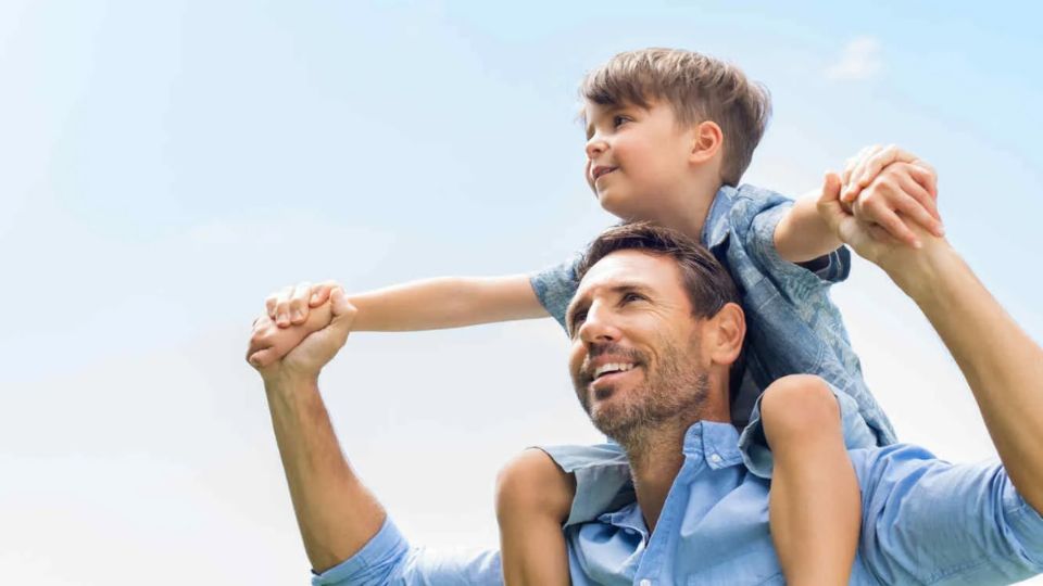 Padre sostiene a uno de sus hijos en sus hombros.
