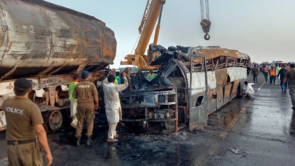 Agentes de policía y trabajadores retiran los restos de un autobús que chocó con un camión cisterna en una autopista en Uch Sharif.