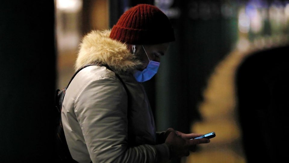 Un joven con cubrebocas textea en su teléfono celular.