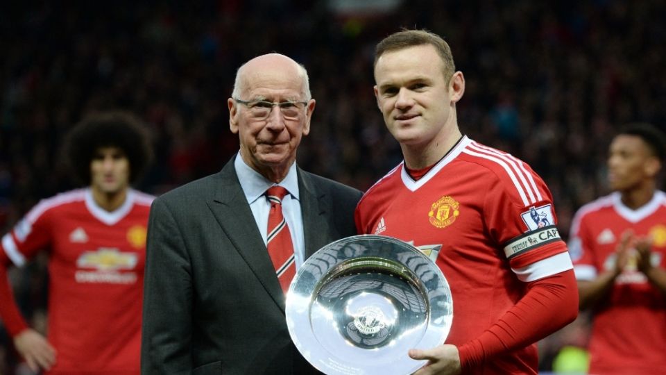 Bobby Charlton y Wayne Rooney sostienen un trofeo.