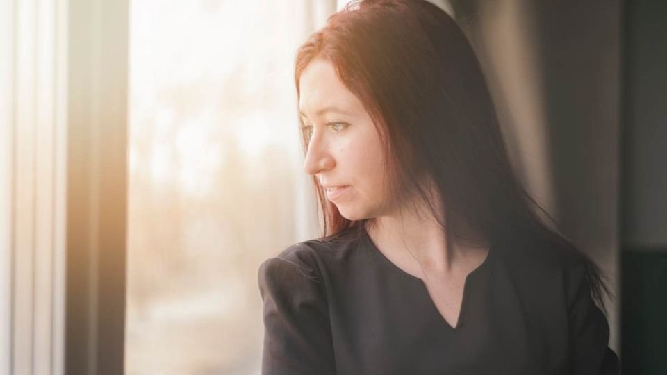 Mujer melancólica observando el atardecer desde su ventana