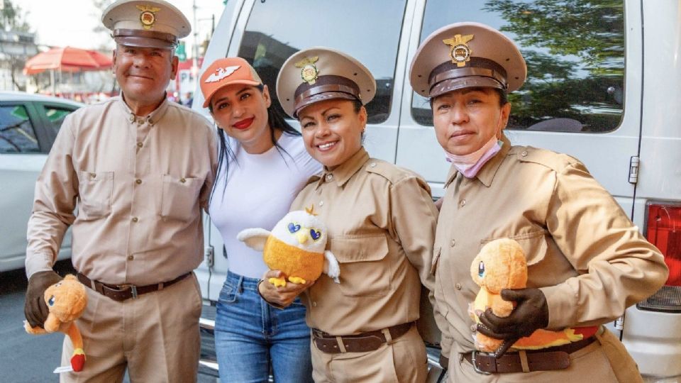 Sandra Cuevas con organilleros, quienes posan con los peluches anaranjados.