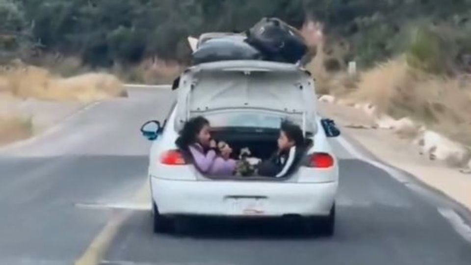 Dos niñas viajando adentro de la cajuela abierta de un automóvil en la carretera de Puebla.